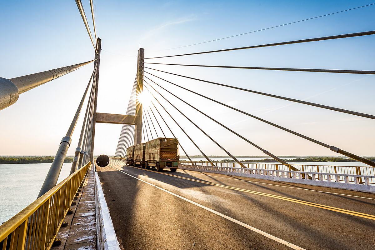 A truck crosses a modern cable-stayed bridge at sunset while the sun shines through the cables onto a river