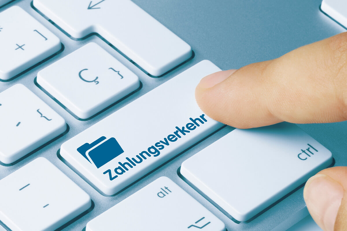 Ein Finger über einer weißen Tastatur, der im Begriff ist, die Taste mit der Aufschrift „Zahlungsverkehr“ und dem blauen Ordnersymbol zu drücken.
